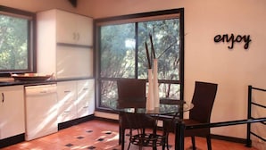 A modern kitchen with white cabinets, a dining table with chairs, and a large window with a view of trees. - Heavenly Retreat - King bed, luxury spa, undercover parking! (Halls Gap)