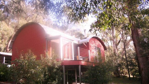 A red house with a covered porch and a small balcony, surrounded by trees and greenery. - Heavenly Retreat - King bed, luxury spa, undercover parking! (Halls Gap)