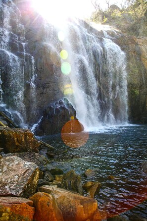 Water cascades over rocky terrain into a serene pool surrounded by boulders.