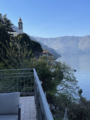 Blick auf einen See mit einem Glockenturm, einem Steinhaus und einem Metallgeländer.