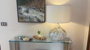 A room with a glass-top desk, a white cushioned bench, a painting of a landscape, and a lamp. - Lake Front with Large Balcony, Lake Access & Boat Dock (NESSO)