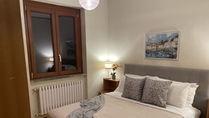 A bedroom with a bed, a window, a radiator, a nightstand, a lamp, and a painting on the wall. - Lake Front with Large Balcony, Lake Access & Boat Dock (NESSO)