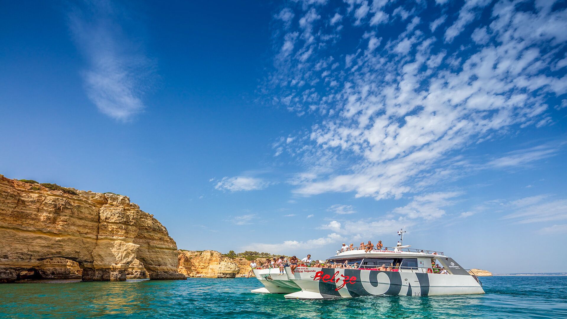 Un bateau transportant des passagers, une côte rocheuse et un ciel bleu dégagé.