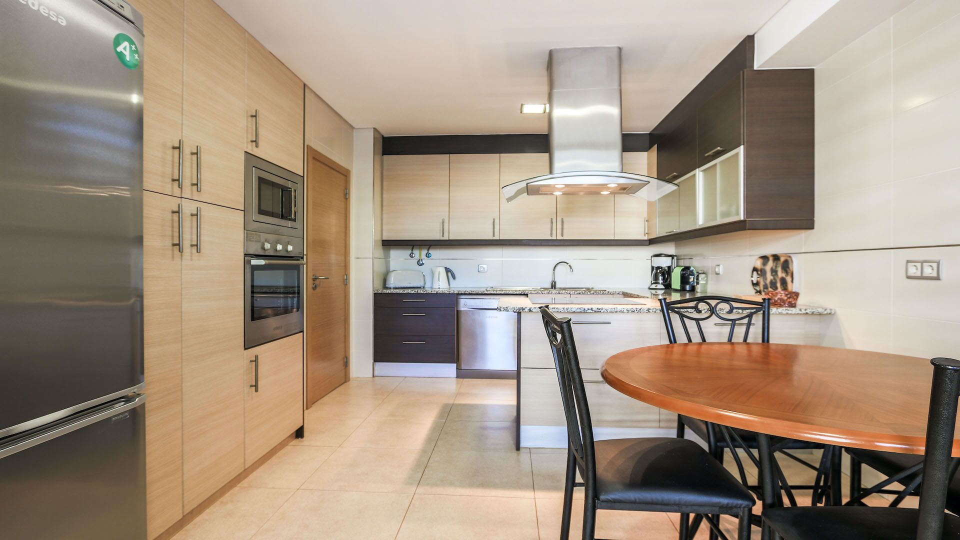 Eine moderne Küche mit Einbauofen, einem Edelstahlkühlschrank und einem Essbereich mit Holztisch und Stühlen.