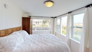 A bedroom with a bed, a wooden headboard, a window with curtains, and a view of the outside.