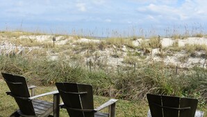 Three wooden chairs facing a beach with sand dunes and sparse vegetation.