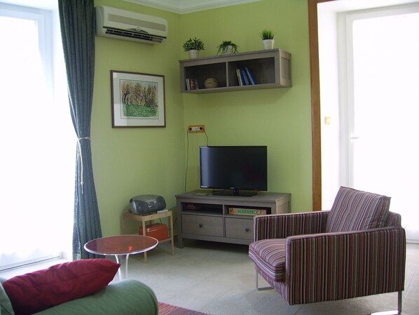 A living room with a television, a striped armchair, a small table, and a bookshelf with plants. - Delightfully furnished, quiet and comfortable, in the historic center (Catania)
