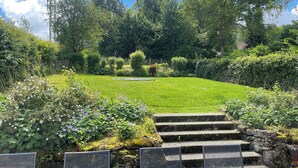 Un jardin bien entretenu, avec une pelouse verdoyante, un petit étang et un escalier en pierre menant à une plateforme d’observation.