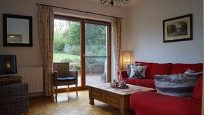 Un salon avec un canapé rouge, une table basse en bois, un fauteuil en osier et un téléviseur.
