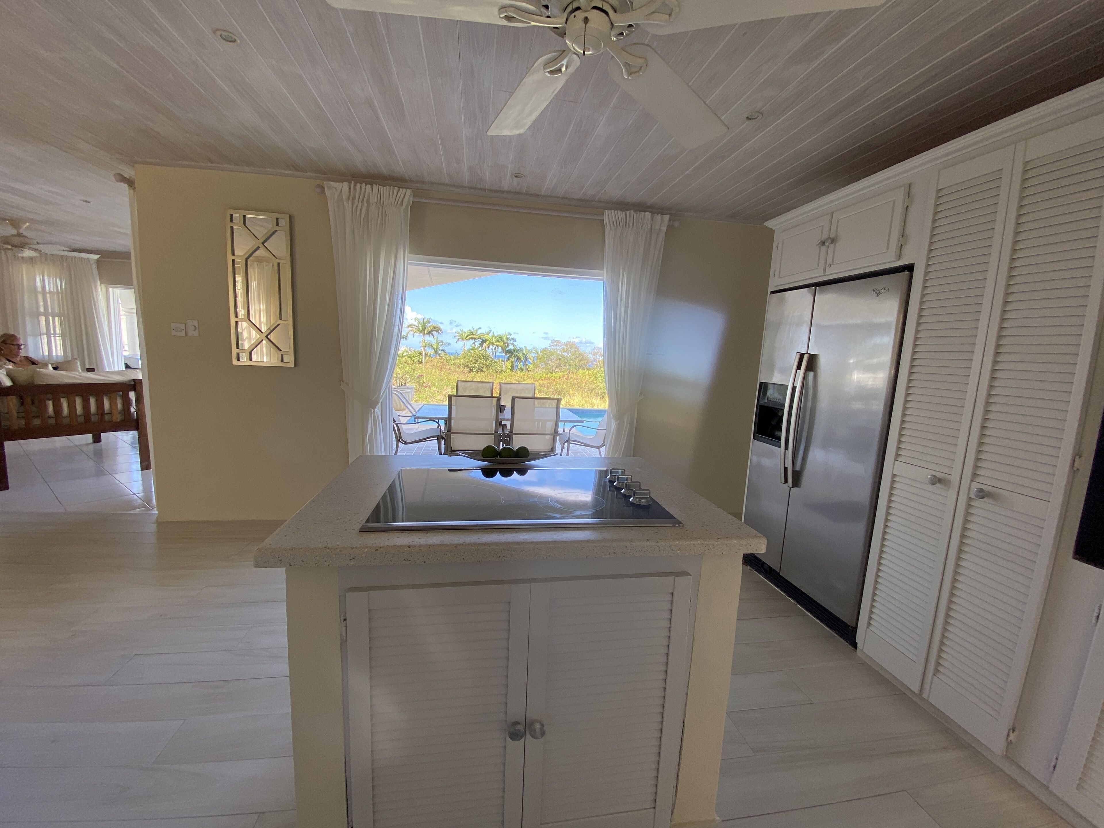 A kitchen with a central island, a refrigerator, and a view of the outdoors.