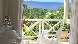 Une vue depuis un balcon doté d’une balustrade blanche, donnant sur un jardin luxuriant et l’océan.