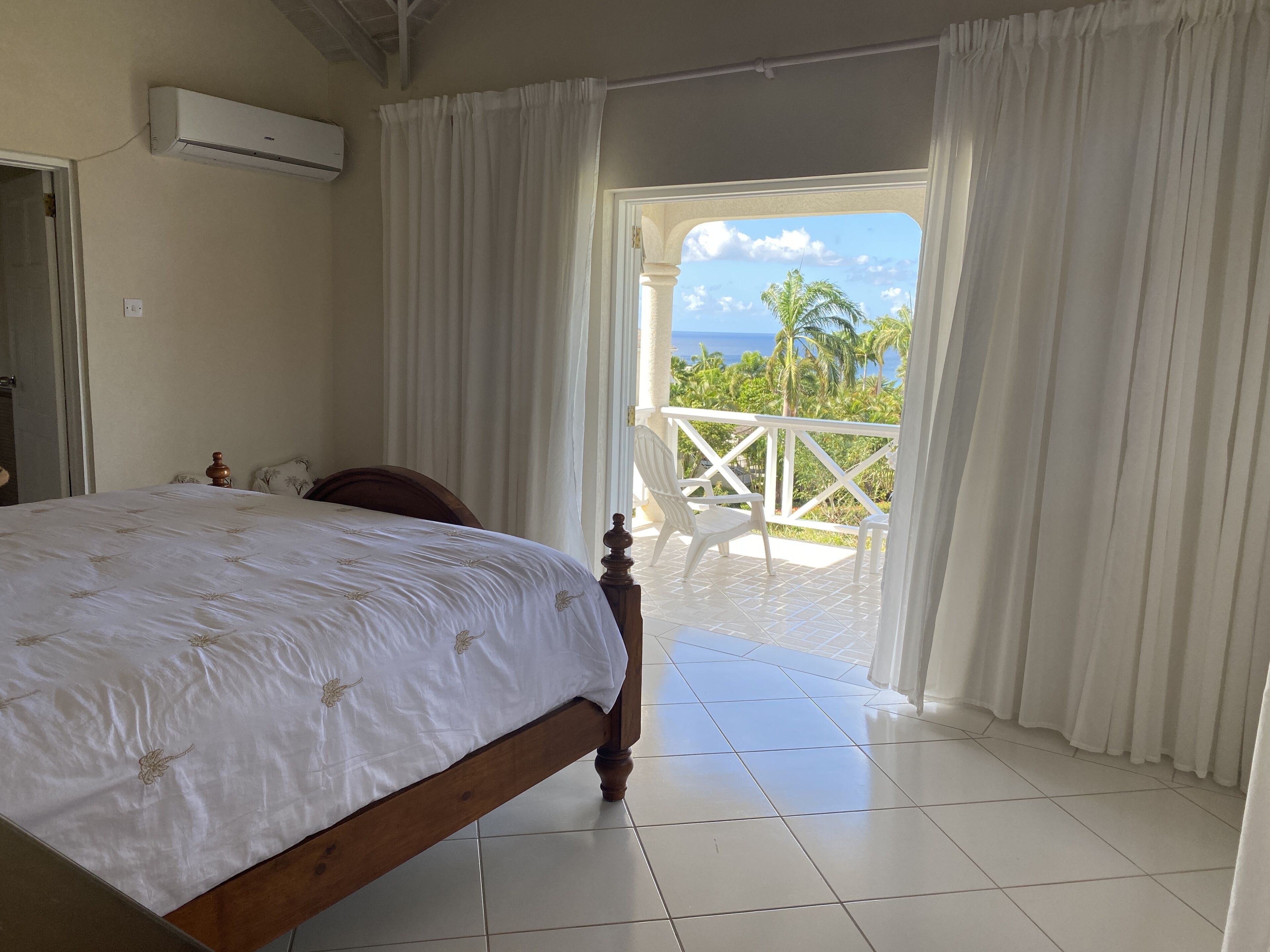 A bedroom with a bed, a view of the ocean, and a balcony with chairs.