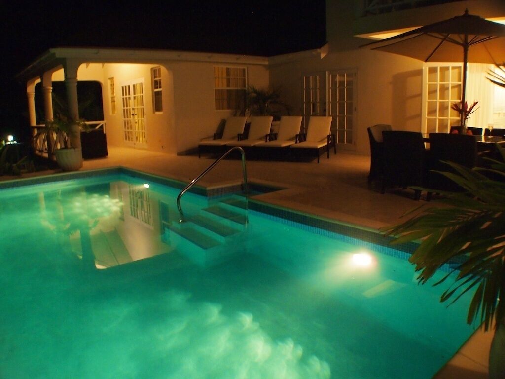A swimming pool with steps leading into it, surrounded by lounge chairs and a covered seating area.