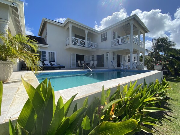 A two-story building with a swimming pool, outdoor seating, and lush greenery.