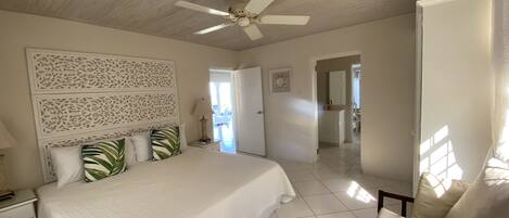 Une chambre spacieuse avec un grand lit, un ventilateur de plafond et une vue sur la salle de bain attenante.