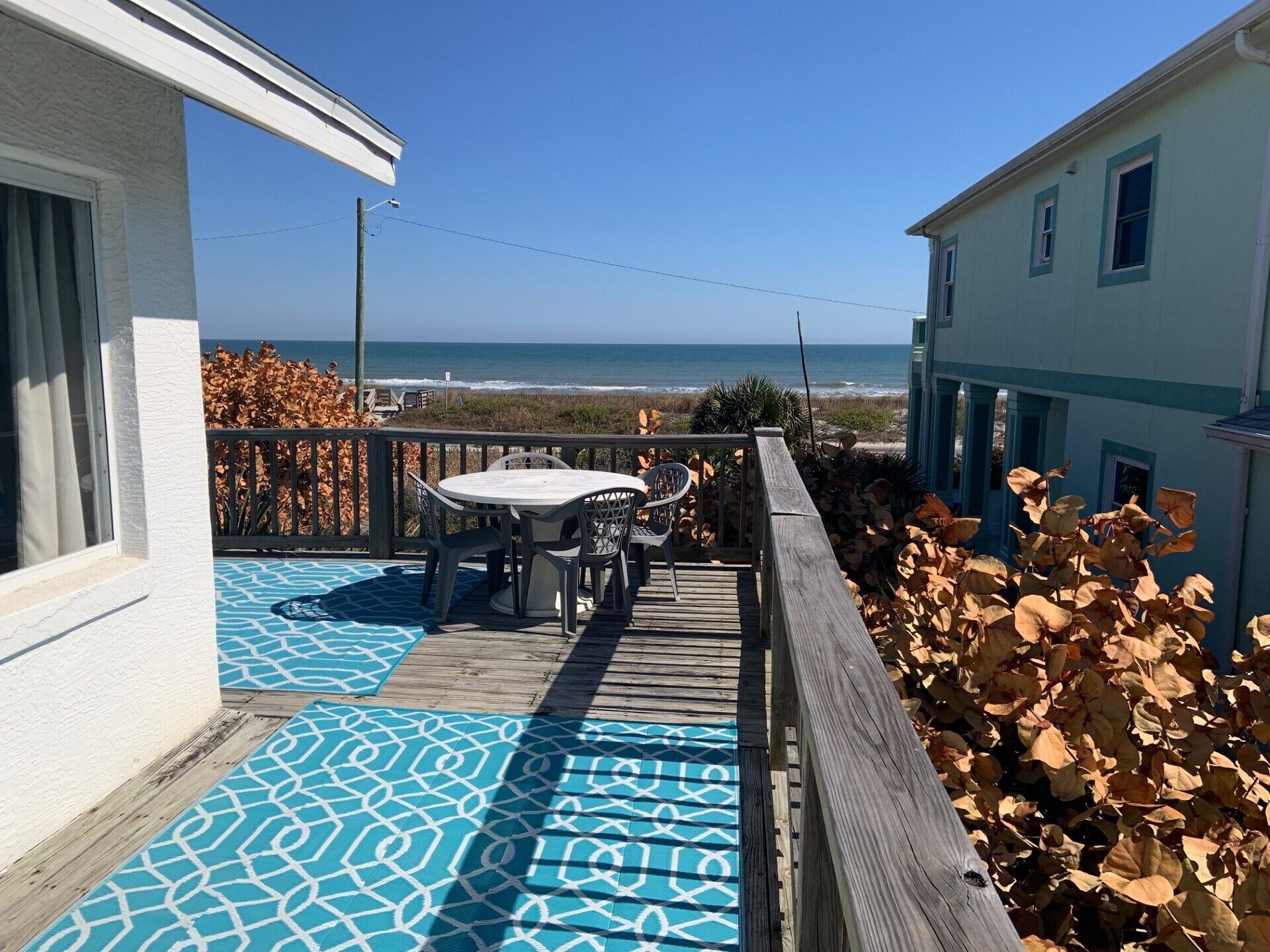 A wooden deck with a table and chairs, overlooking a beach.