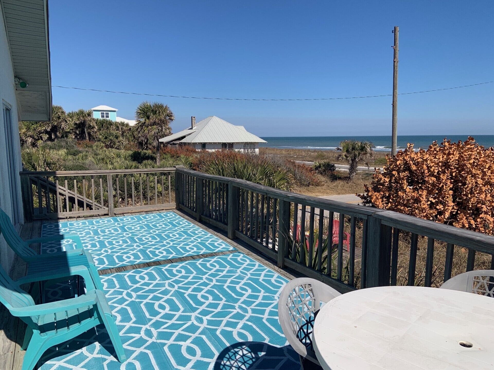 Un balcón con suelo estampado, una mesa y sillas, con vista a una playa y al océano.