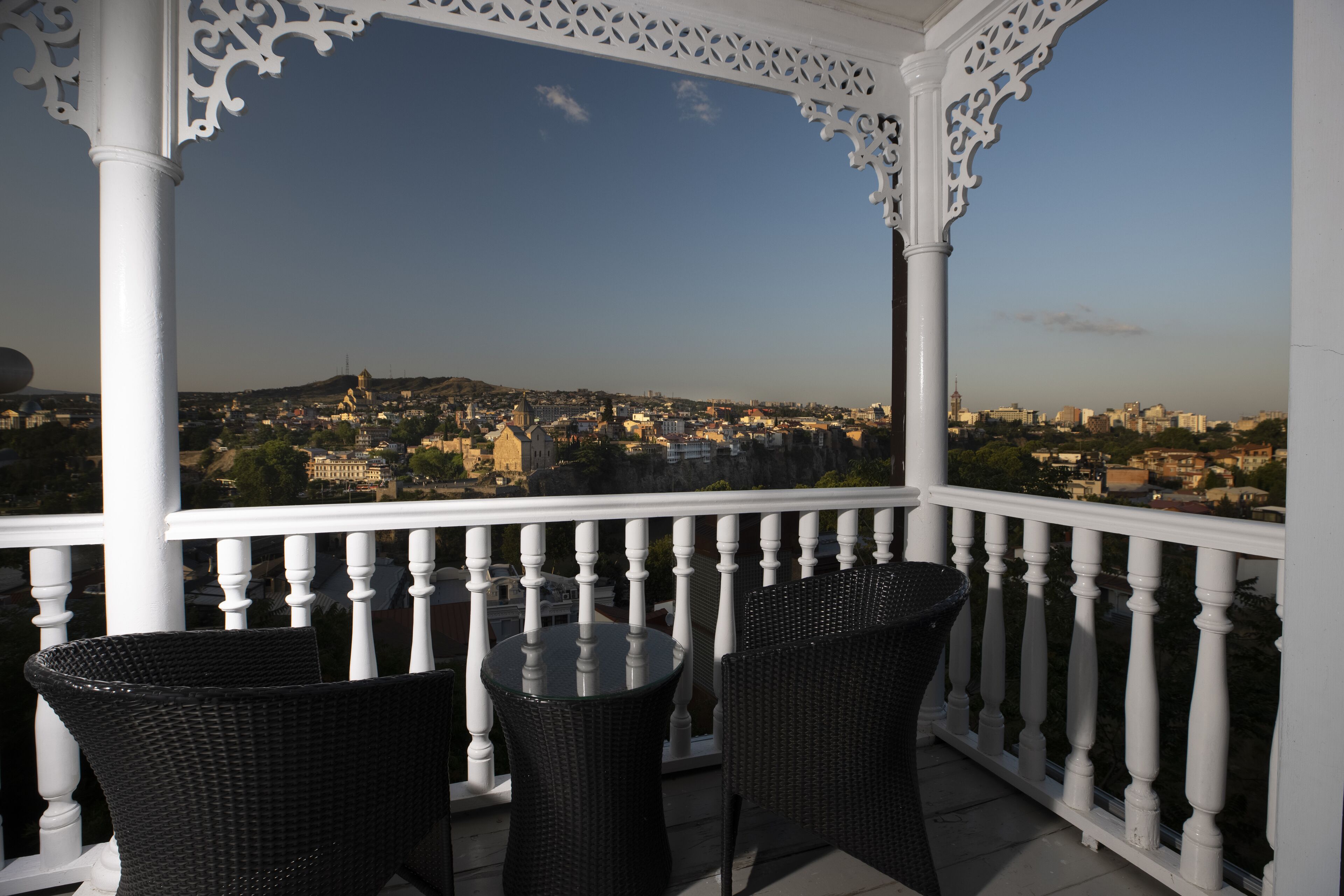 A balcony with white balustrades and wicker furniture overlooking a cityscape.