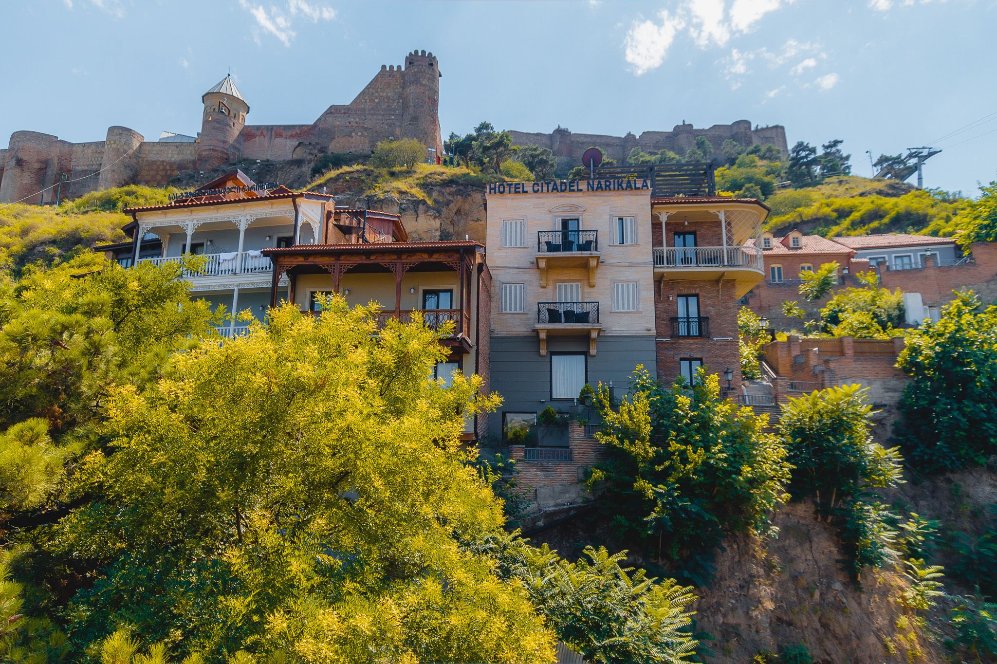 Un hotel con balcón, vistas a un castillo y abundante vegetación.