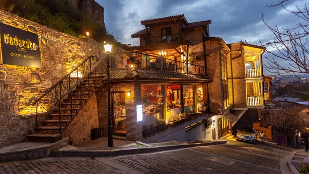 A stone building with a staircase leading to a second-floor balcony. - Citadel Narikala Hotel (Tbilisi)