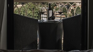 A balcony with wicker furniture, a bottle of wine, and two glasses. In the background, there's a view of a cityscape with a prominent building with a golden dome. - Citadel Narikala Hotel (Tbilisi)