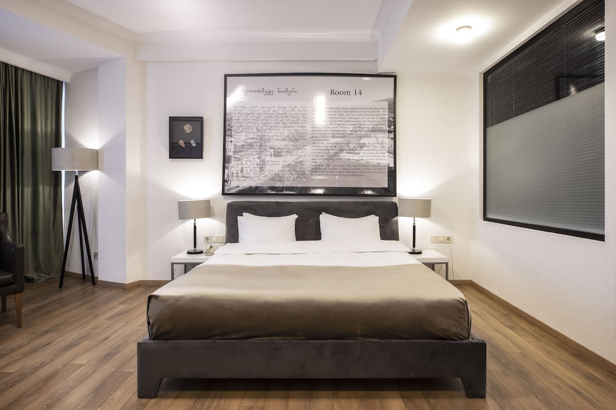 A modern hotel room with a large bed, two bedside tables, a desk, and a large framed text on the wall.