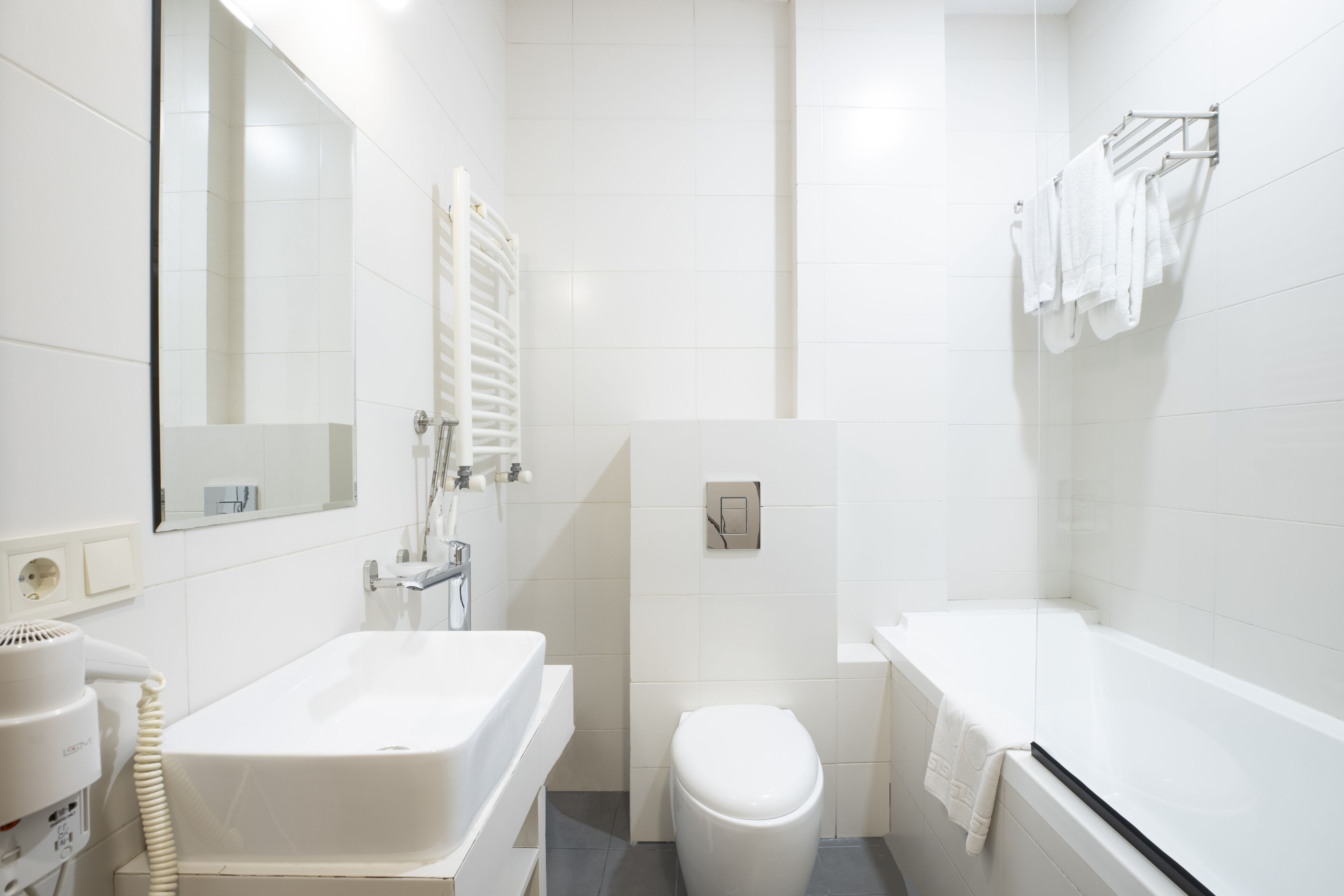 A bathroom with a white sink, toilet, and bathtub. There is a towel rack with towels hanging on it.