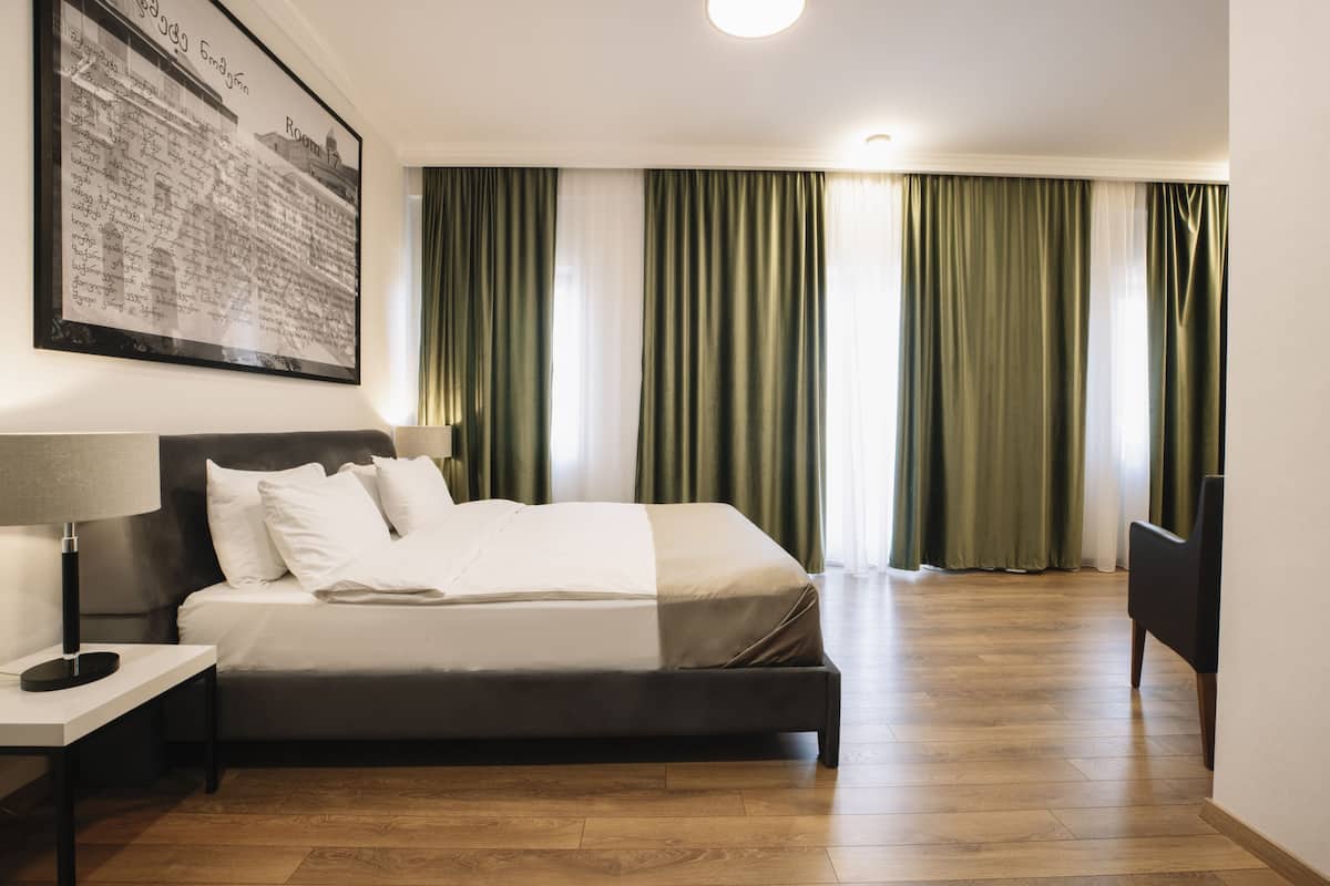 A hotel room with a bed, a nightstand, a lamp, and a large framed picture on the wall.