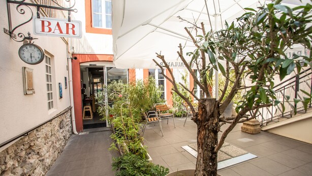 A courtyard with a bar sign, outdoor seating, and potted plants.