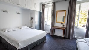 A hotel room with a large bed, a desk, a mirror, and a view of the outdoors.