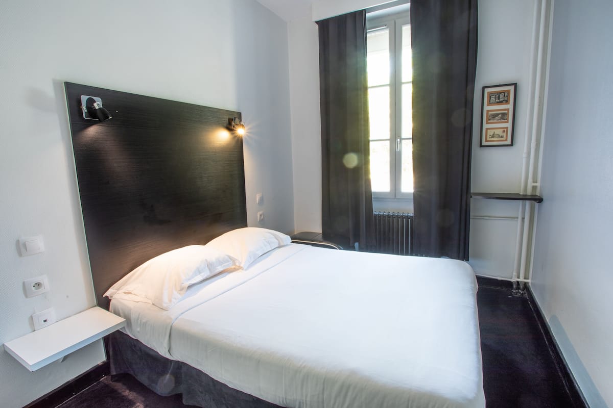 Een moderne hotelkamer met een groot bed, een nachtkastje, een wandlamp en een raam met gordijnen.