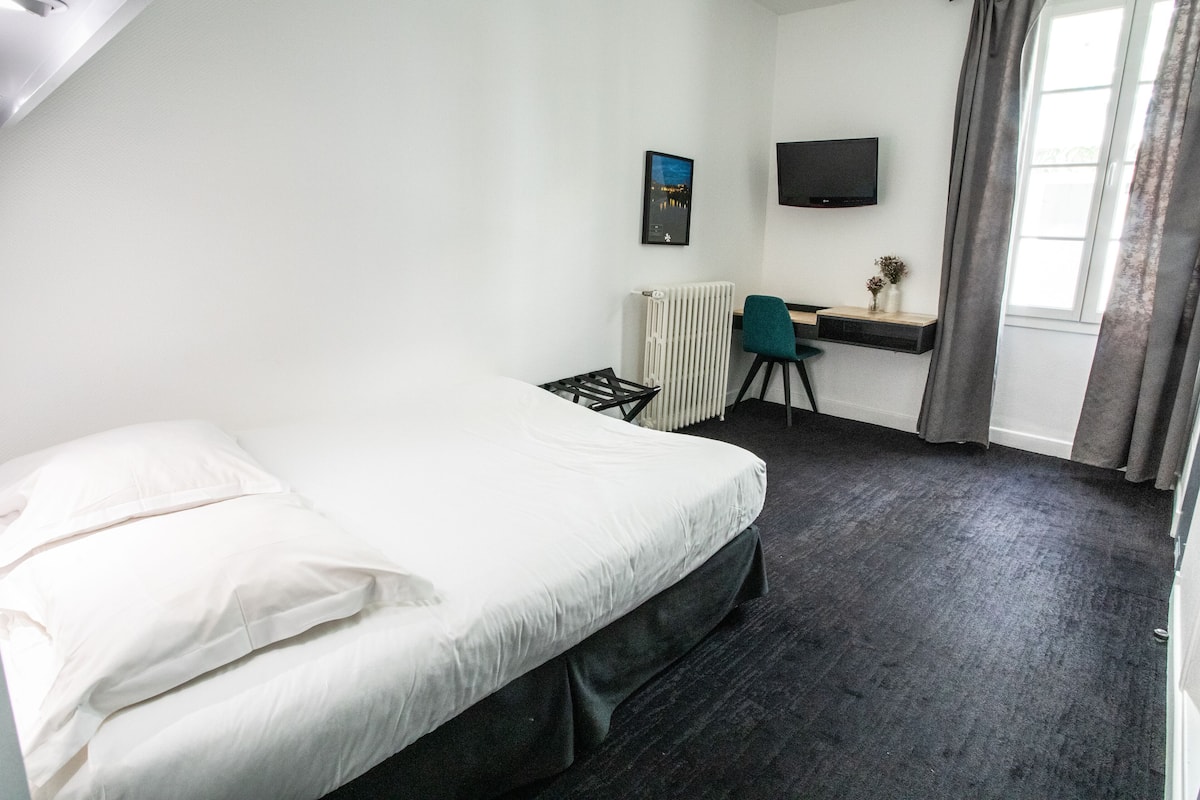 Hotelkamer met een bed, bureau met stoel, radiator, televisie aan de muur en raam met gordijnen.