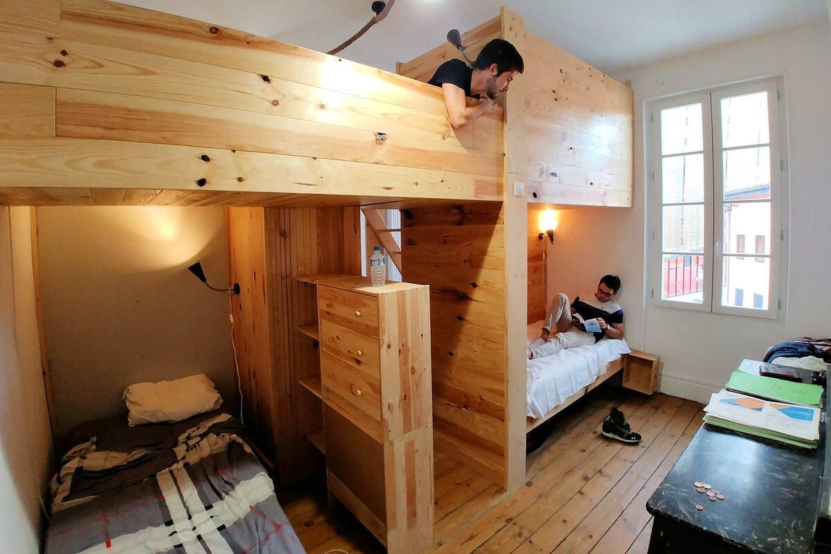 Une petite pièce comprenant un lit superposé, un bureau et une fenêtre.