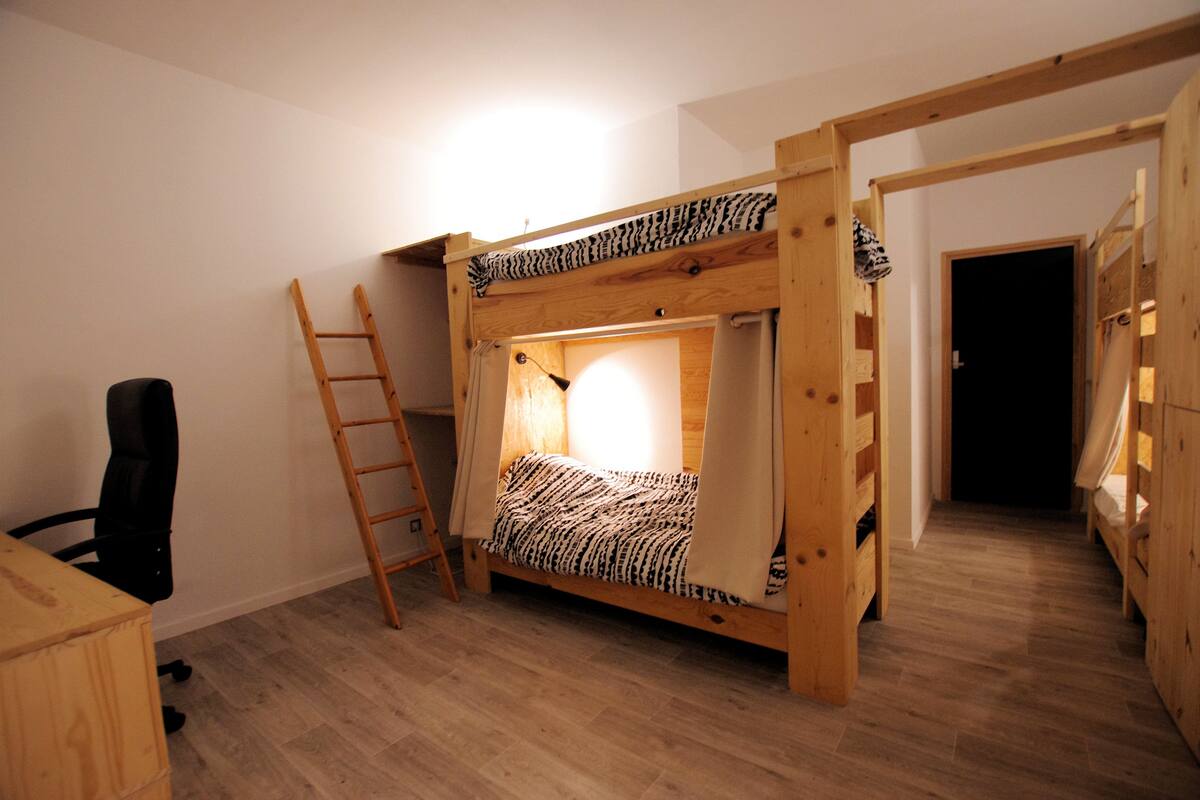 Une chambre avec un lit superposé, une échelle, un bureau et une chaise.