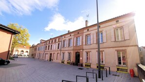 A paved courtyard with a row of buildings featuring traditional architecture, a clear sky, and a parked car. - Hostel les Cordées Liées (Albi)