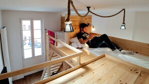 A room with a bunk bed, a wooden staircase, and a window with a view of parked cars. - Hostel les Cordées Liées (Albi)