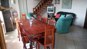 A dining area with a wooden table and chairs, a sofa, a television, and a staircase.