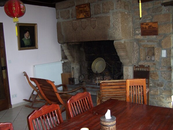 A dining area with a stone fireplace, wooden chairs, a table, and a red lantern.