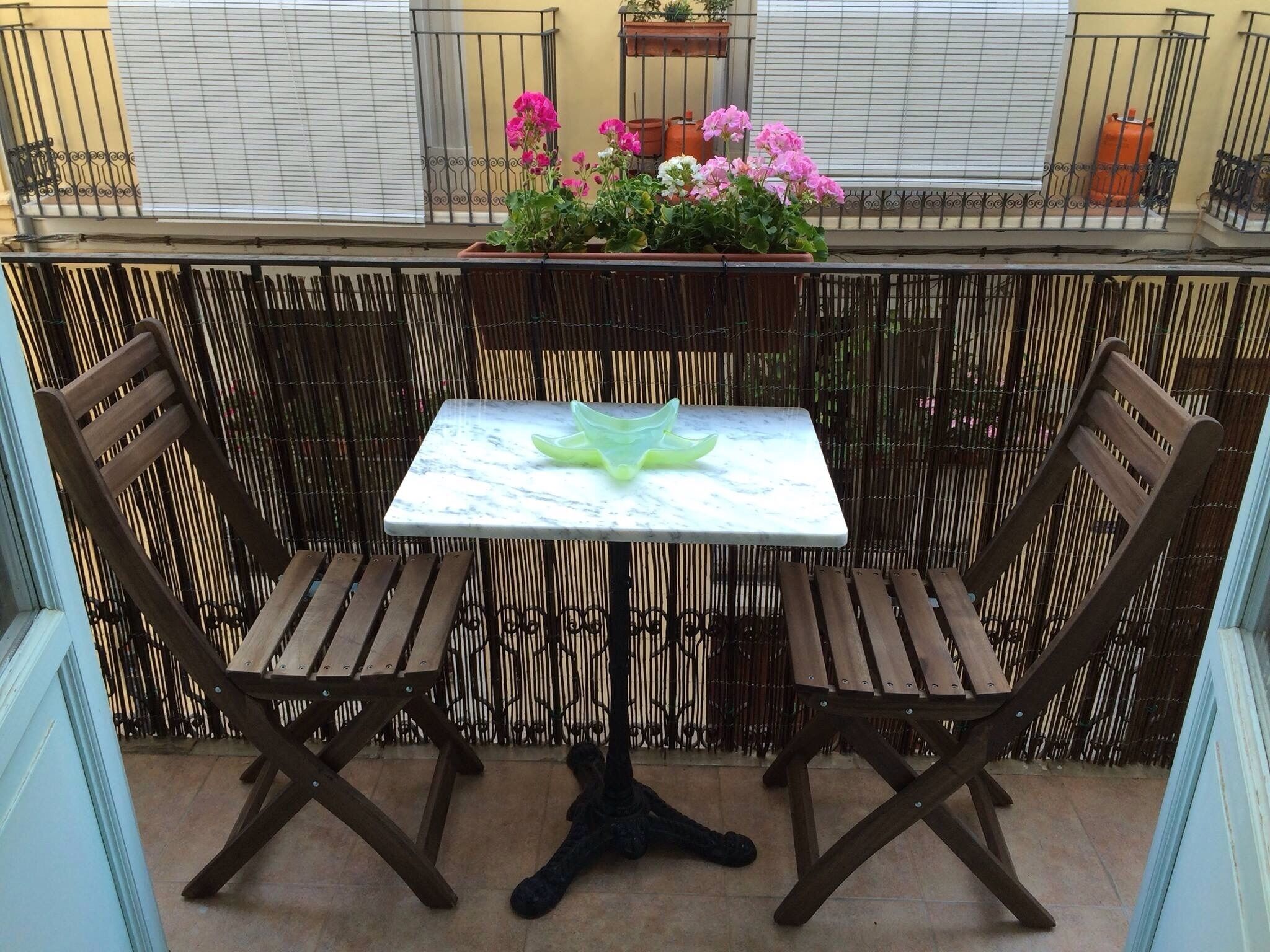 A balcony with a small table and two wooden chairs, surrounded by a bamboo fence.
