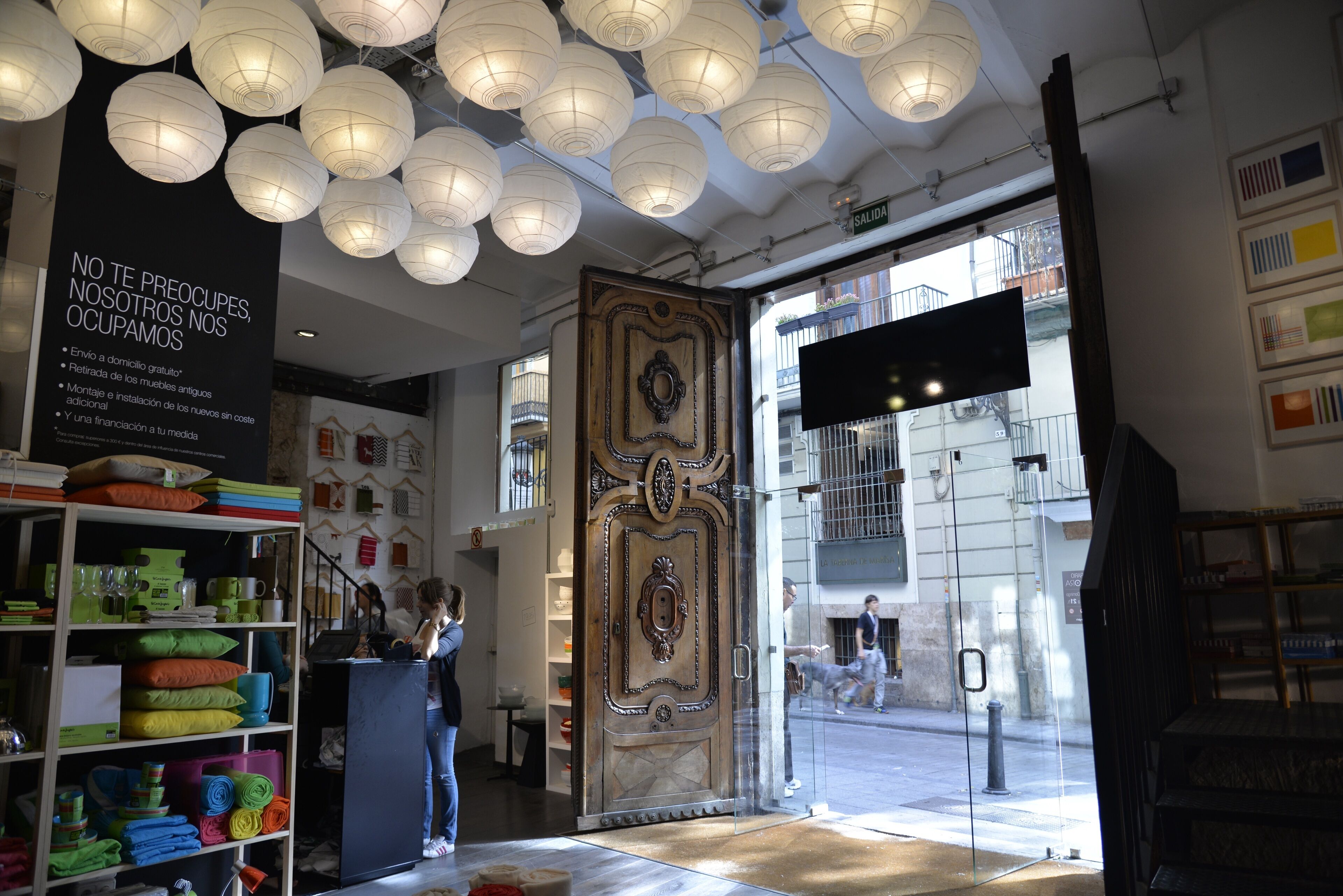 Interior de una tienda con estantes llenos de almohadas coloridas, una puerta decorativa grande y farolillos de papel colgantes.