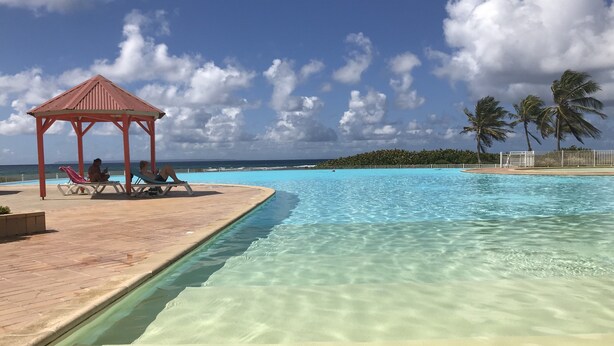 En klarblå pool med ett trädäck och en lusthus.
