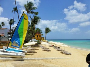 A beach with lounge chairs and umbrellas, a sailboat, and a small wooden structure. - Stunning & spacious 3 bed villa, Own pool, housekeeper, 3 Min walk to beach. (Porters)