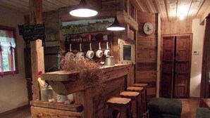 Uma área de bar rústica com balcão de madeira, banquetas, um relógio e uma placa com texto.