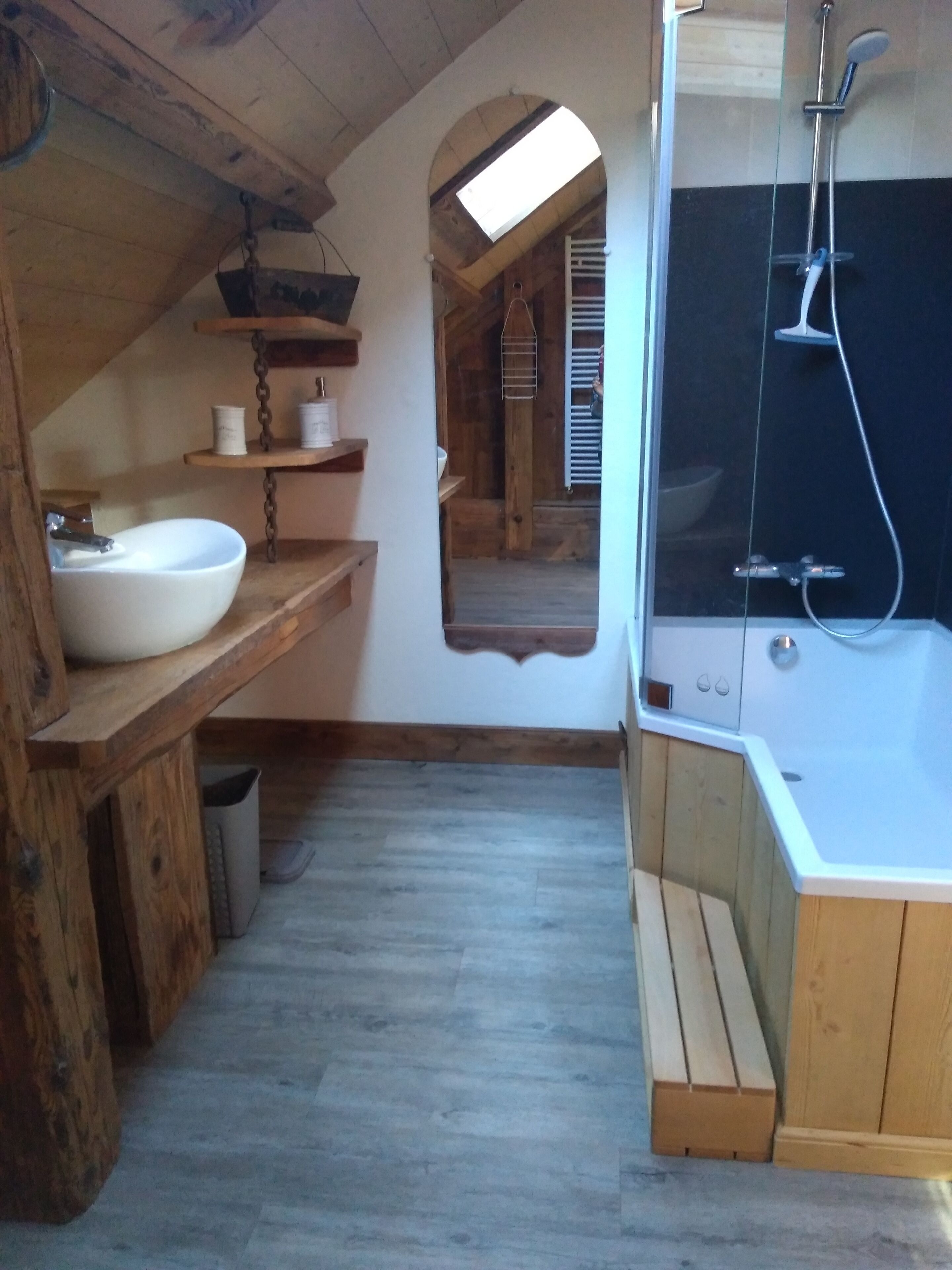 A rustic bathroom with a wooden vanity, a white sink, and a shower area.