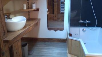 A rustic bathroom with a wooden vanity, a white sink, and a shower area.