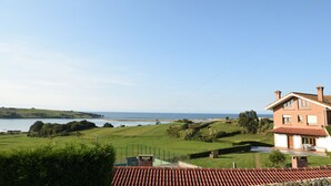 A two-story house with a red-tiled roof, a front porch, and a view of the sea.