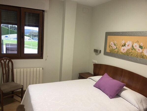 A bedroom with a bed, a chair, a radiator, a window with a view, and a wall-mounted light fixture. - Luxury apartment with swimming-pool and tennis court. Beach 600m. (Mogro)