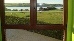 A view through a wooden-framed window with a view of a green landscape and a body of water.
