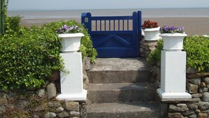 A blue gate leading to a beach, flanked by white pillars with purple flowers. - Beachside Cottage Idyllic Situation, Stunning Views Over Morecambe Bay (Baycliff, Ulverston)