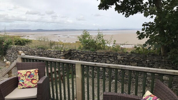 A wicker outdoor seating area with a glass table, two chairs, and a view of a beach and distant hills. - Beachside Cottage Idyllic Situation, Stunning Views Over Morecambe Bay (Baycliff, Ulverston)
